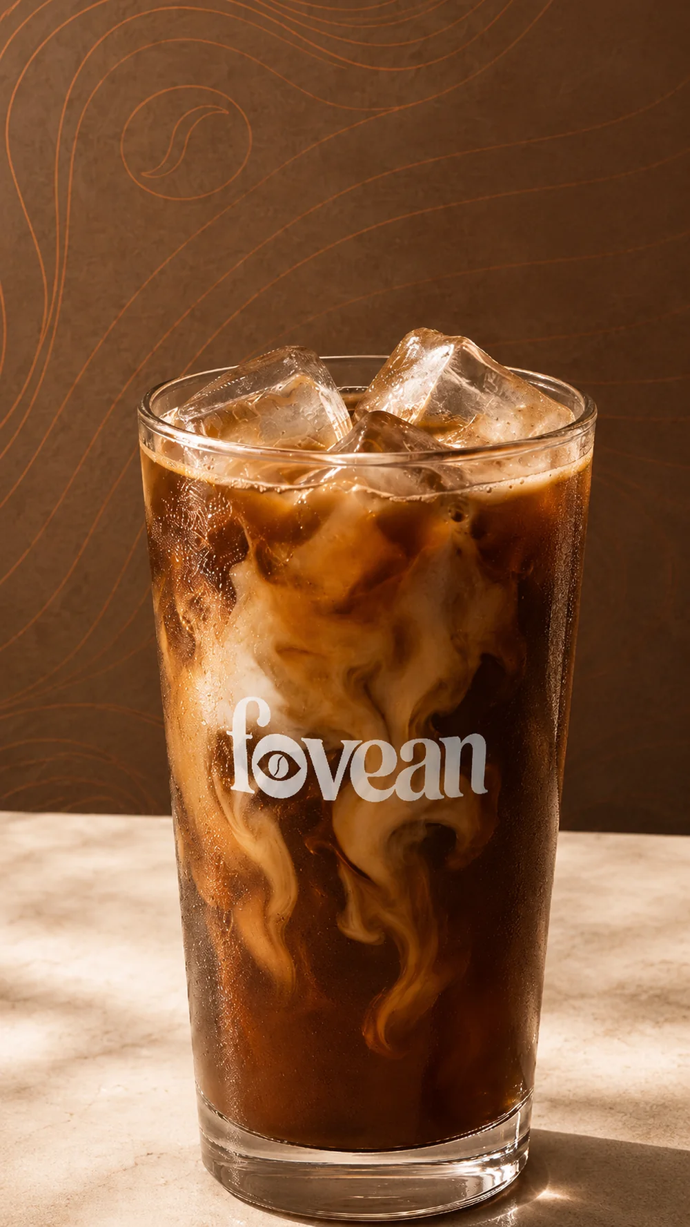 A tall FOVEAN-branded glass of iced coffee with the logo optically centered on the glass, cream swirling through the ice